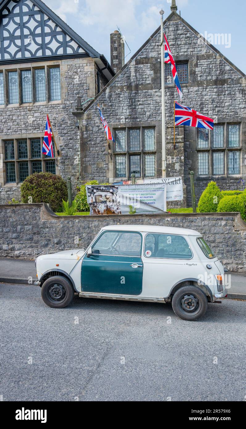 Classic white British Leyland mini mayfair car with green door parked outside a stone built building with the union flags. Stock Photo