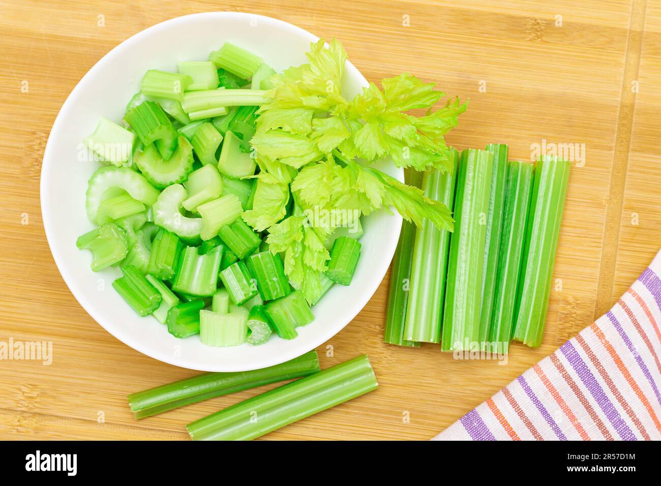 Fresh Chopped Celery Slices in White Bowl with Celery Sticks on Bamboo