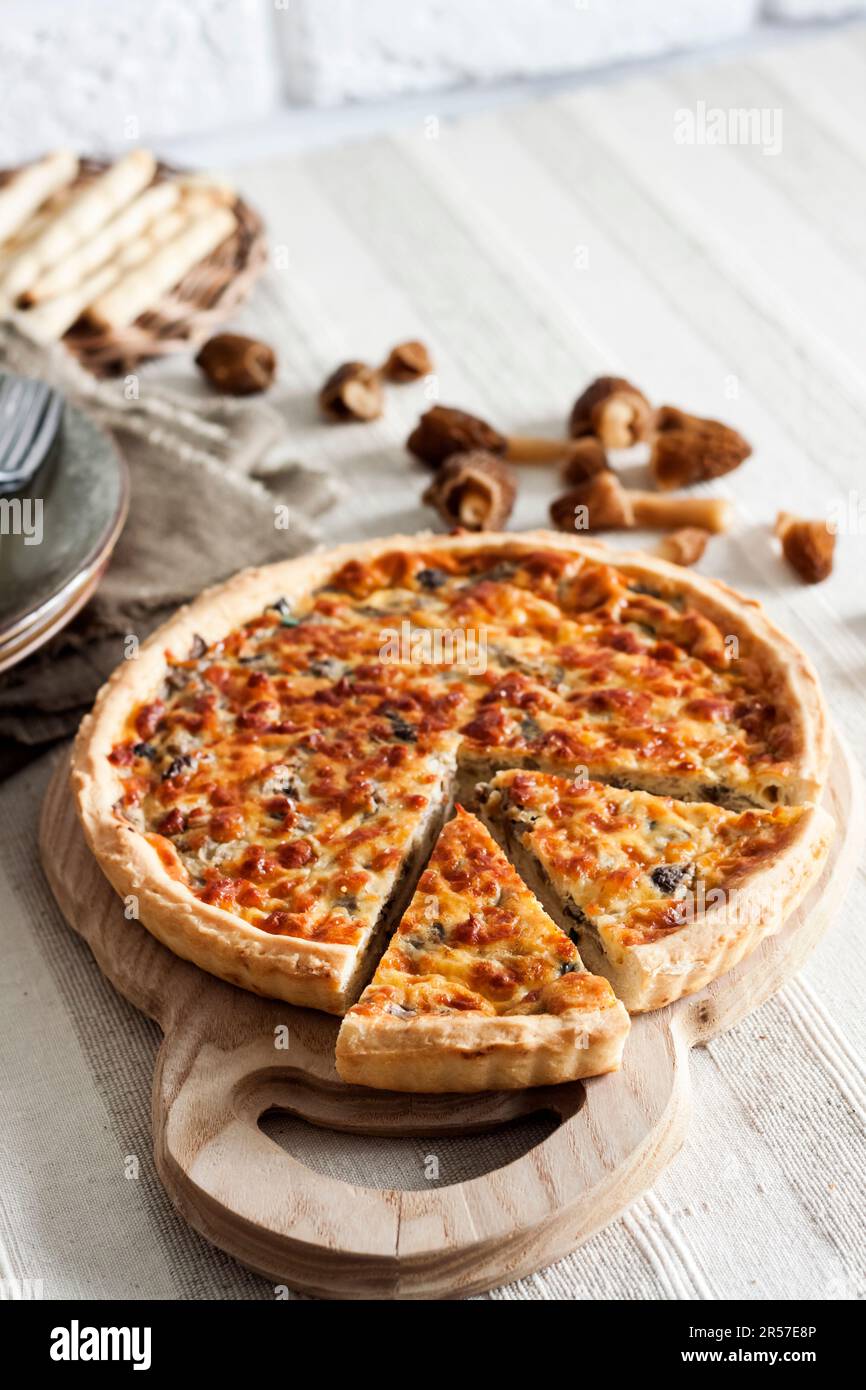 Quiche - open tart pie with morel mushrooms, onion and mozzarella cheese on wooden cutting board Stock Photo