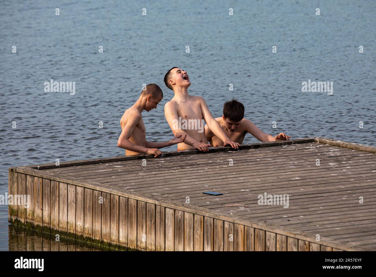Teenage boys standing in cold water by jetty in Töölönlahti Bay, Helsinki, Finland Stock Photo