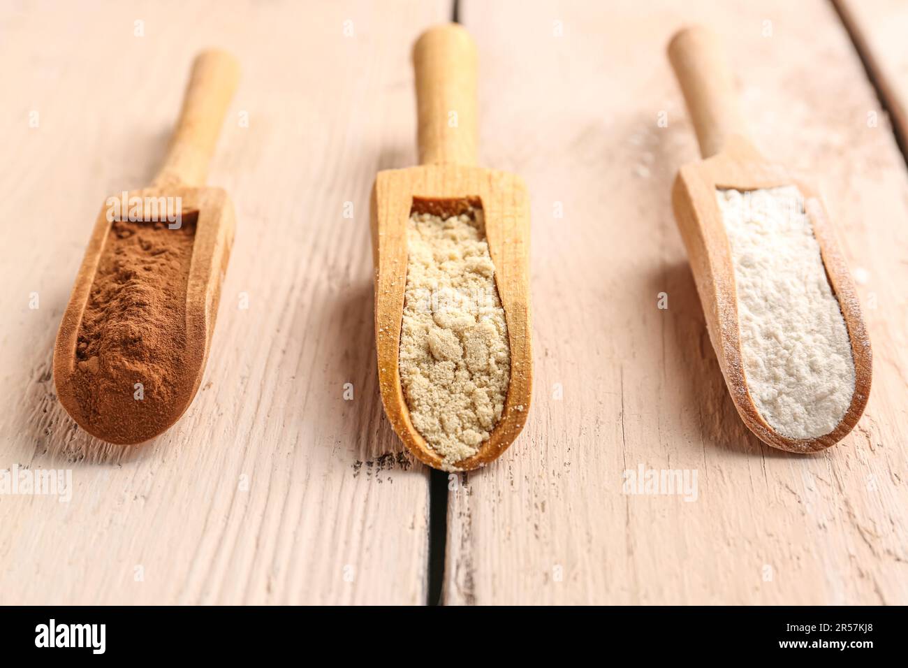 Wooden scoops with different types of flour and cacao on light wooden