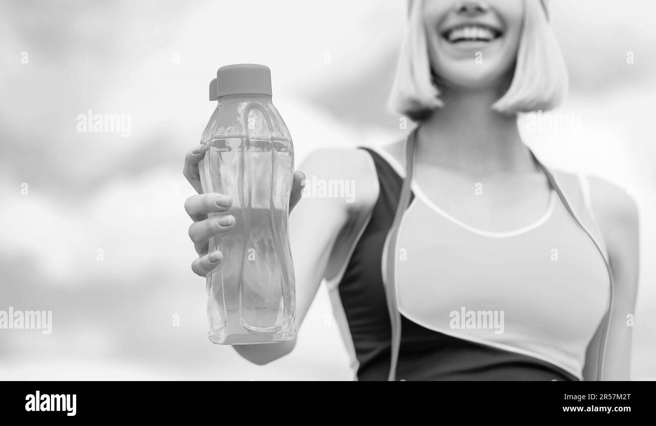 Woman drinking water after run. Sports girl drinks water from a bottle on a sky background. Drinking during sport. Black and white Stock Photo
