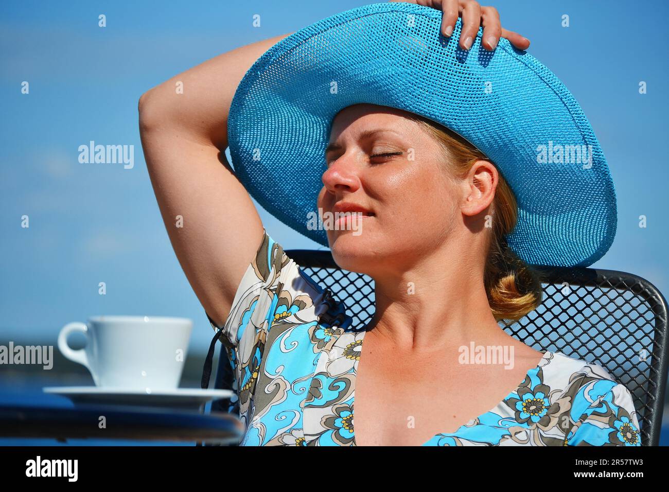 Young woman with the blue hat having coffee on the beach Stock Photo