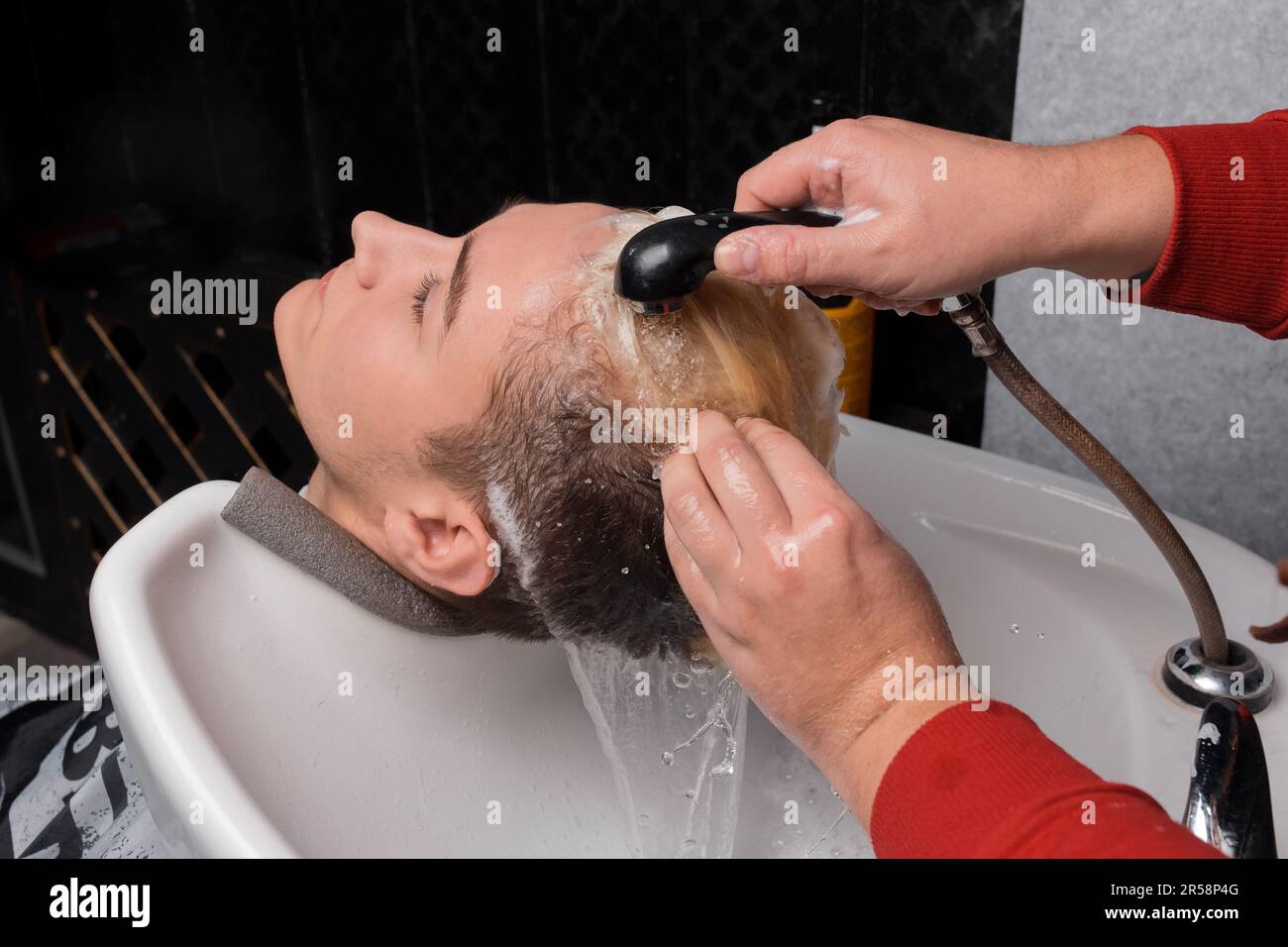 The hands of a professional barbershop worker wash the head and hair of a client, a young guy in the sink before a haircut. Stock Photo