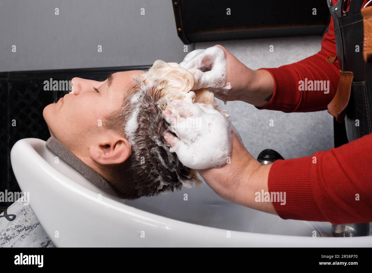 The hands of a professional barber wash the client's hair and hair with