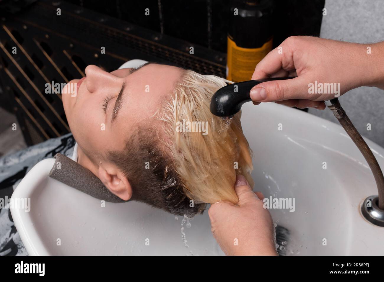 Washing the head and hair of a client of a young handsome guy in the sink in a professional barbershop hairdresser. Stock Photo