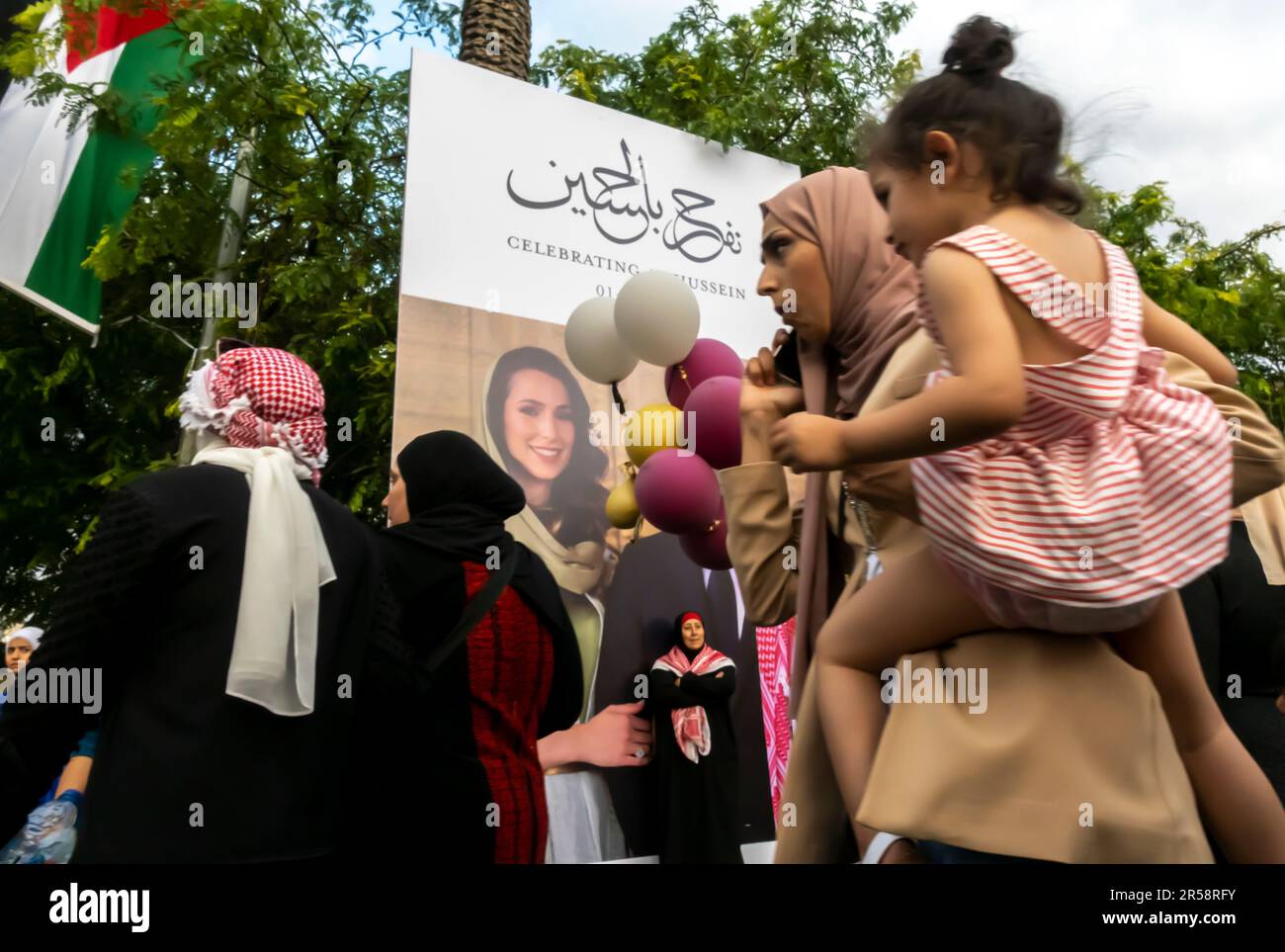 Jordanian woman carryin her child girl by the banner with Rajwa Al Saif poster. June 1, 2023. Amman Jordan Stock Photo