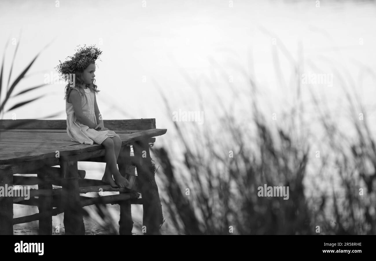 Cute little girl wearing wreath made of beautiful flowers on pier near ...