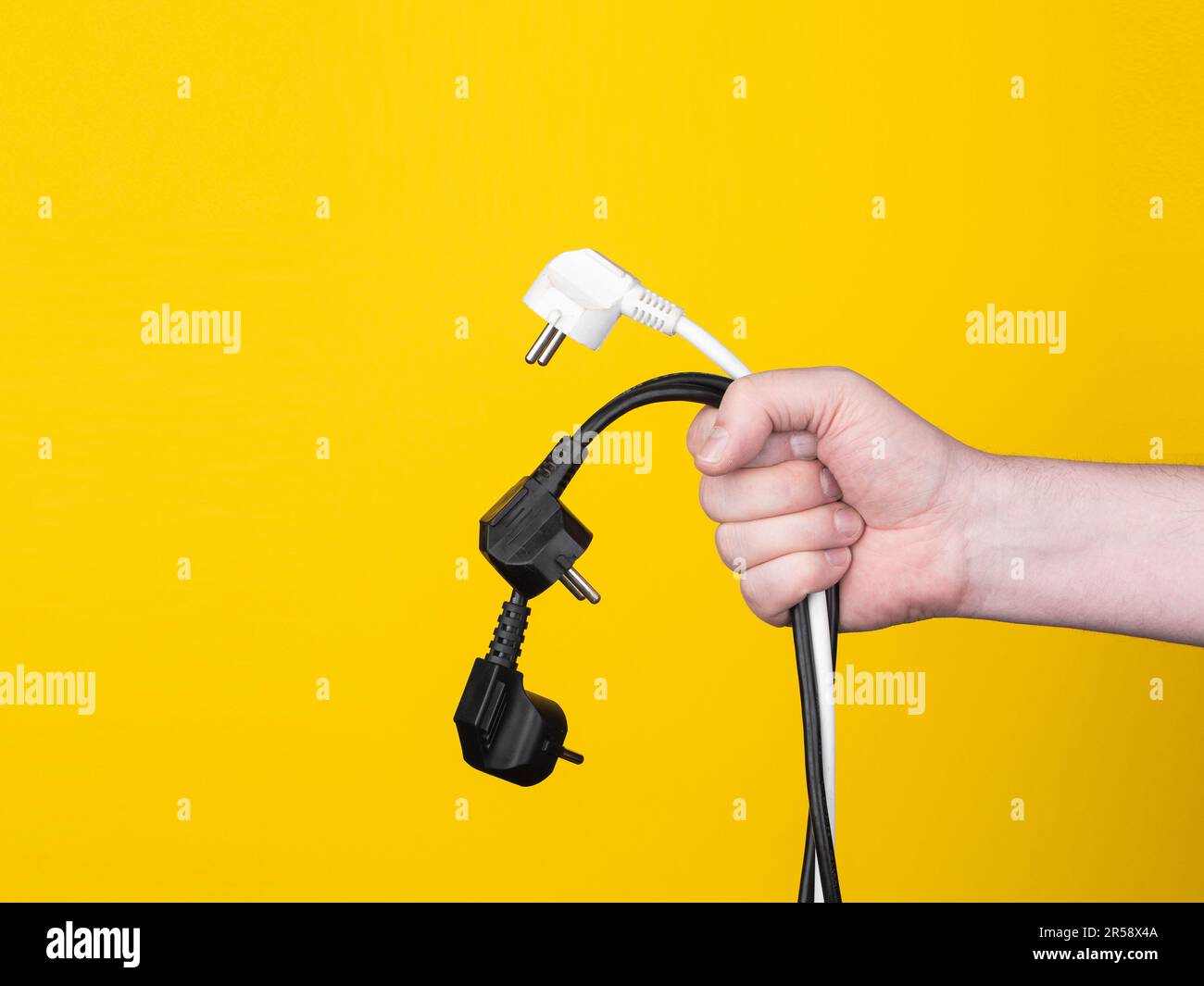 A male hand holds three electric plugs. No face, yellow background, copy space. Stock Photo