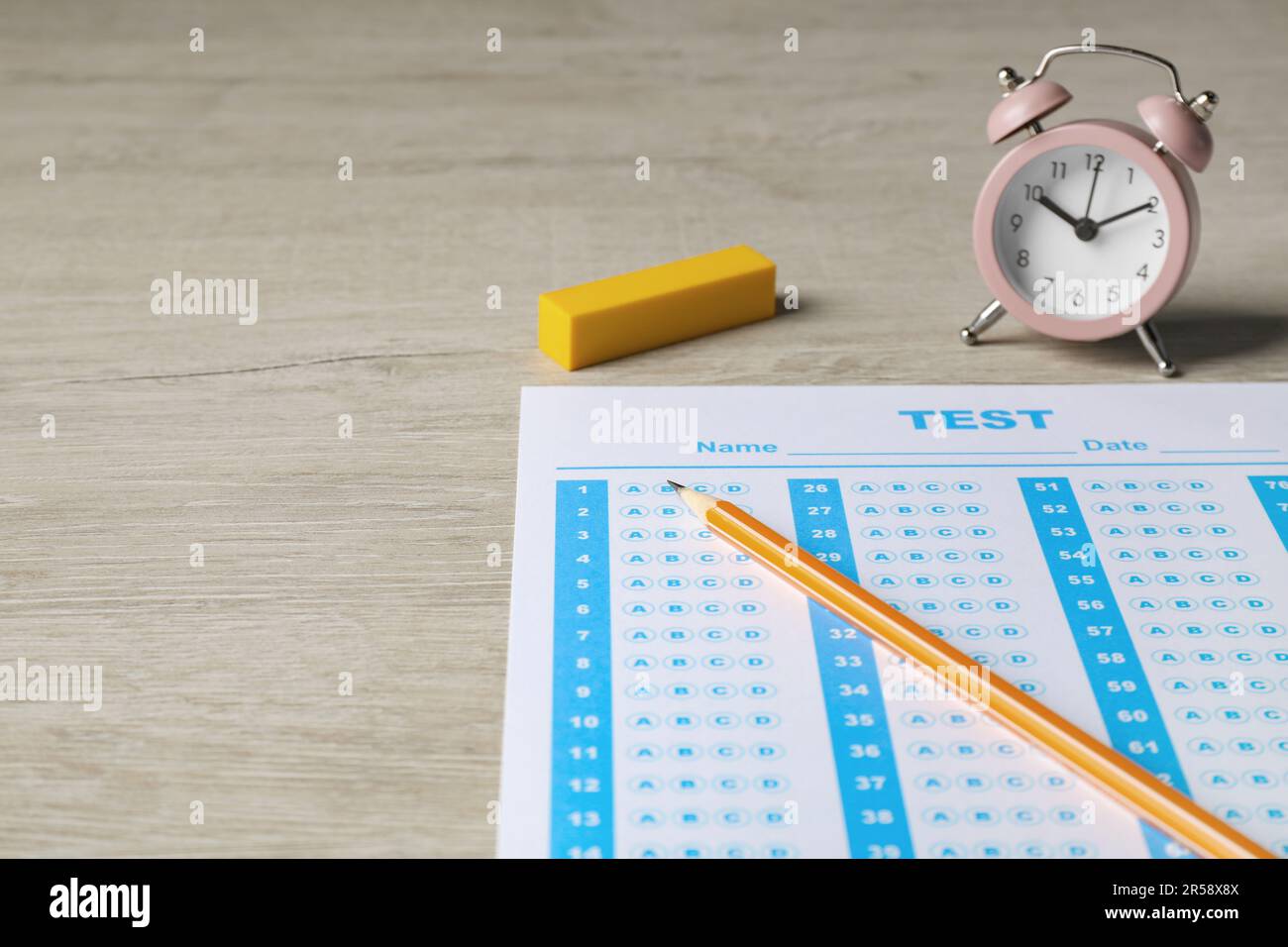 Answer sheet, pencil and alarm clock on wooden table, space for text