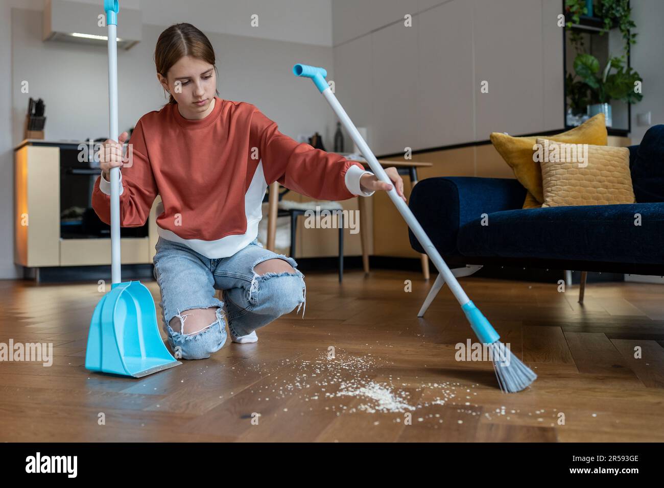 Focused teen girl sweep floor in living room from scattered debris with