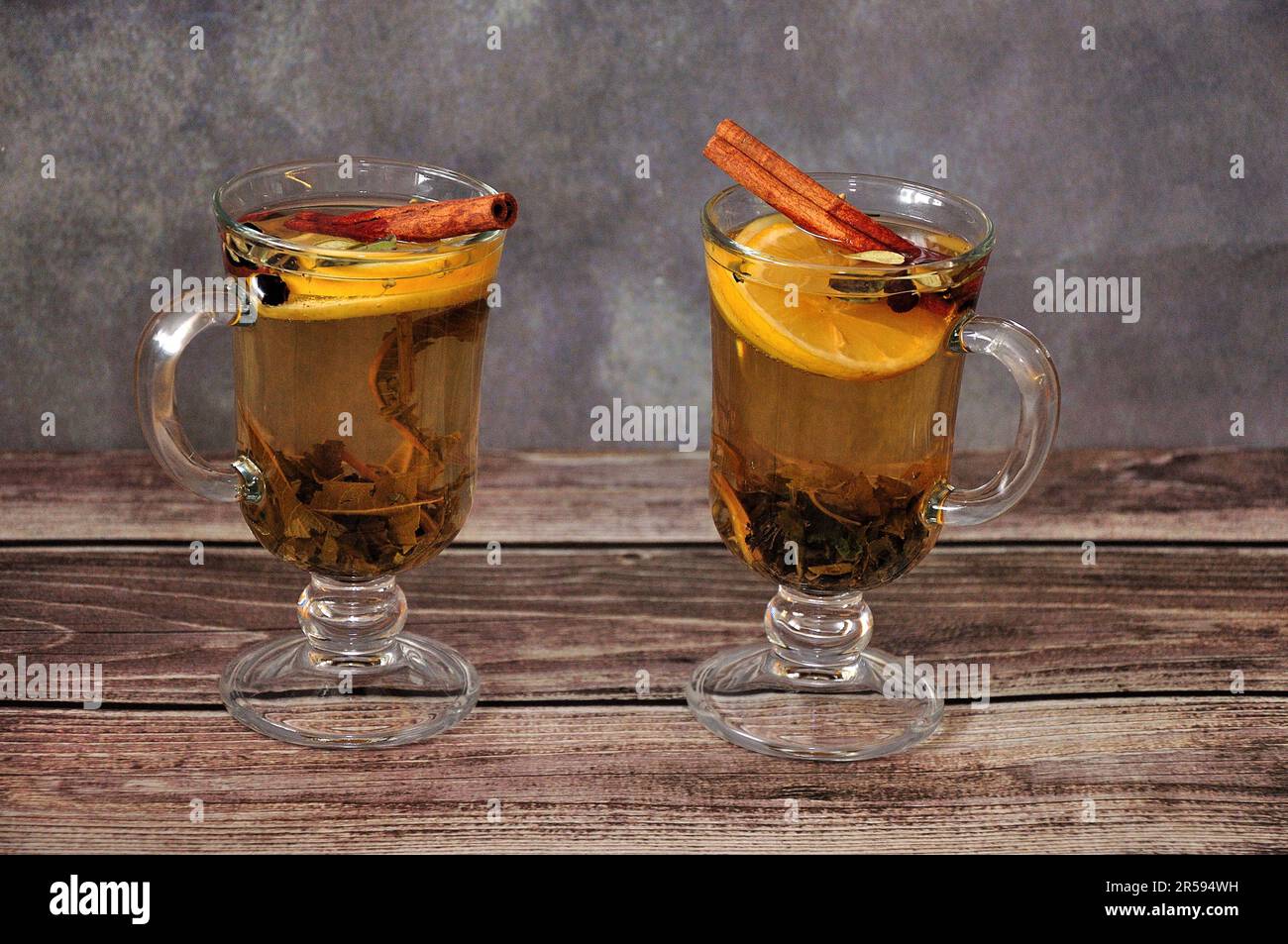 Two glasses of hot herbal tea with lemon slice, spices and cinnamon sticks on a wooden table. Close-up. Stock Photo