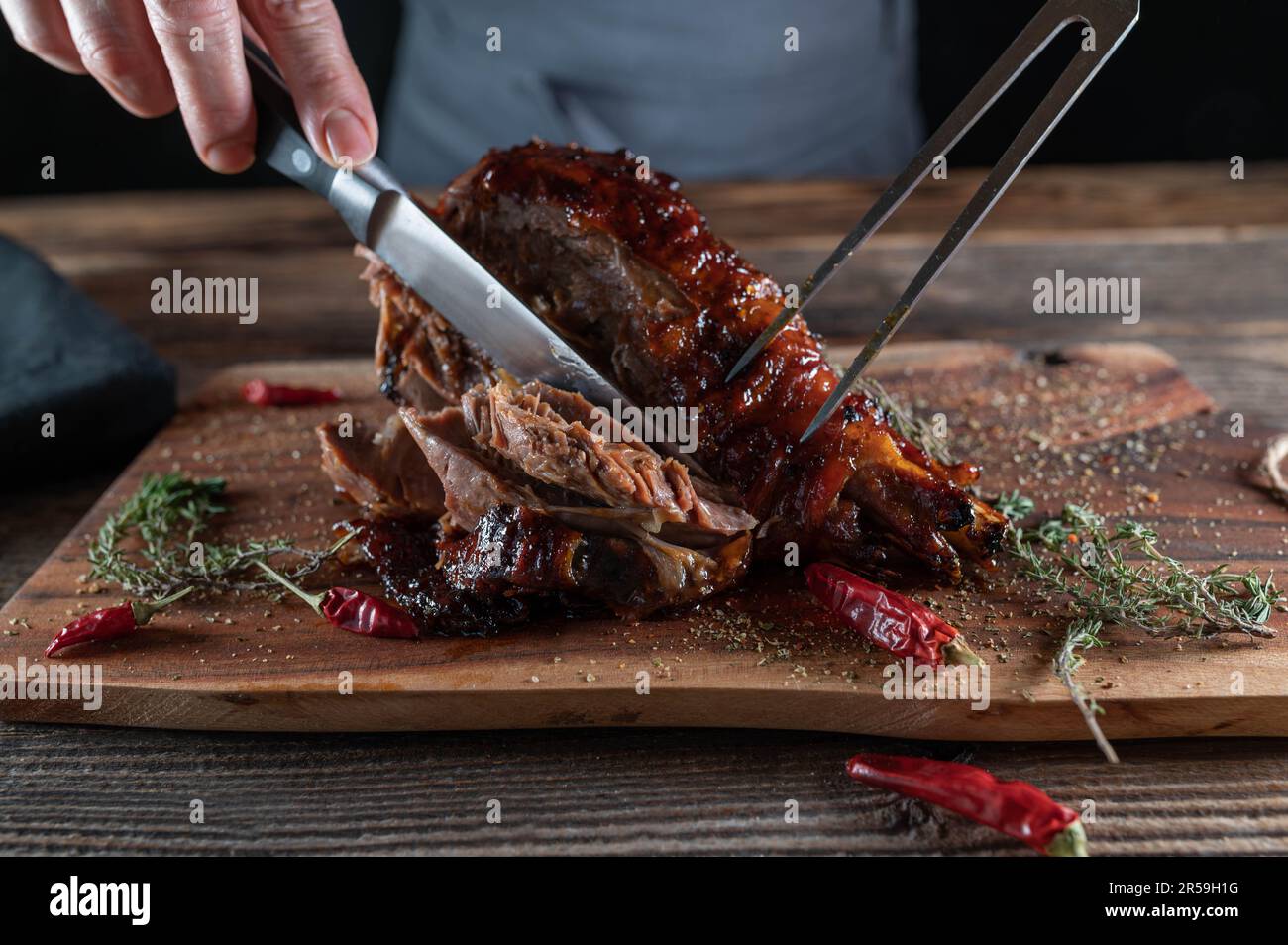 Smoked turkey leg on wooden cutting board is getting sliced with knife and meat fork Stock Photo