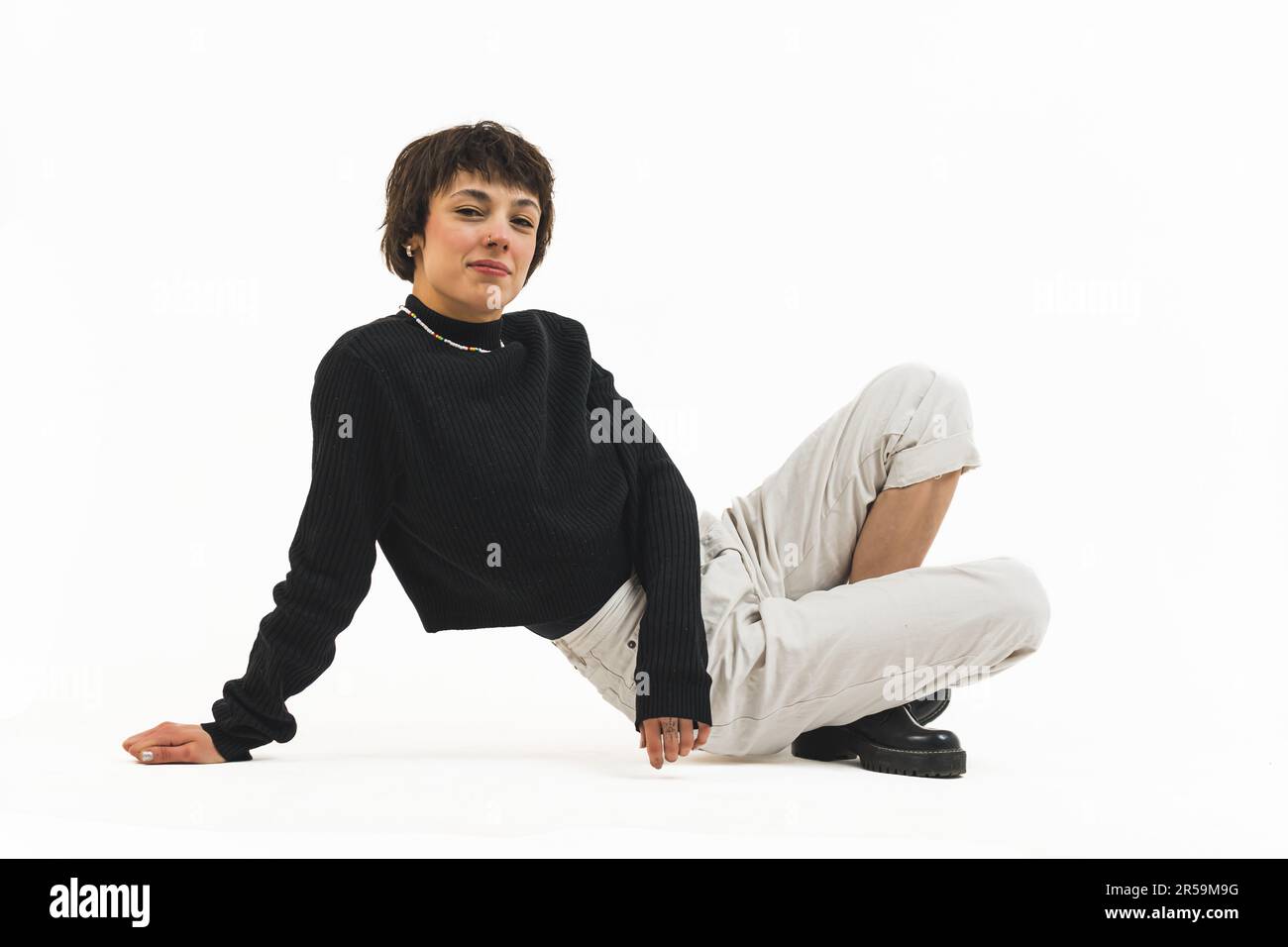 Full shot of a woman in a black jumper and white trousers sitting with her legs crossed and leaning one hand on the ground. High quality photo Stock Photo