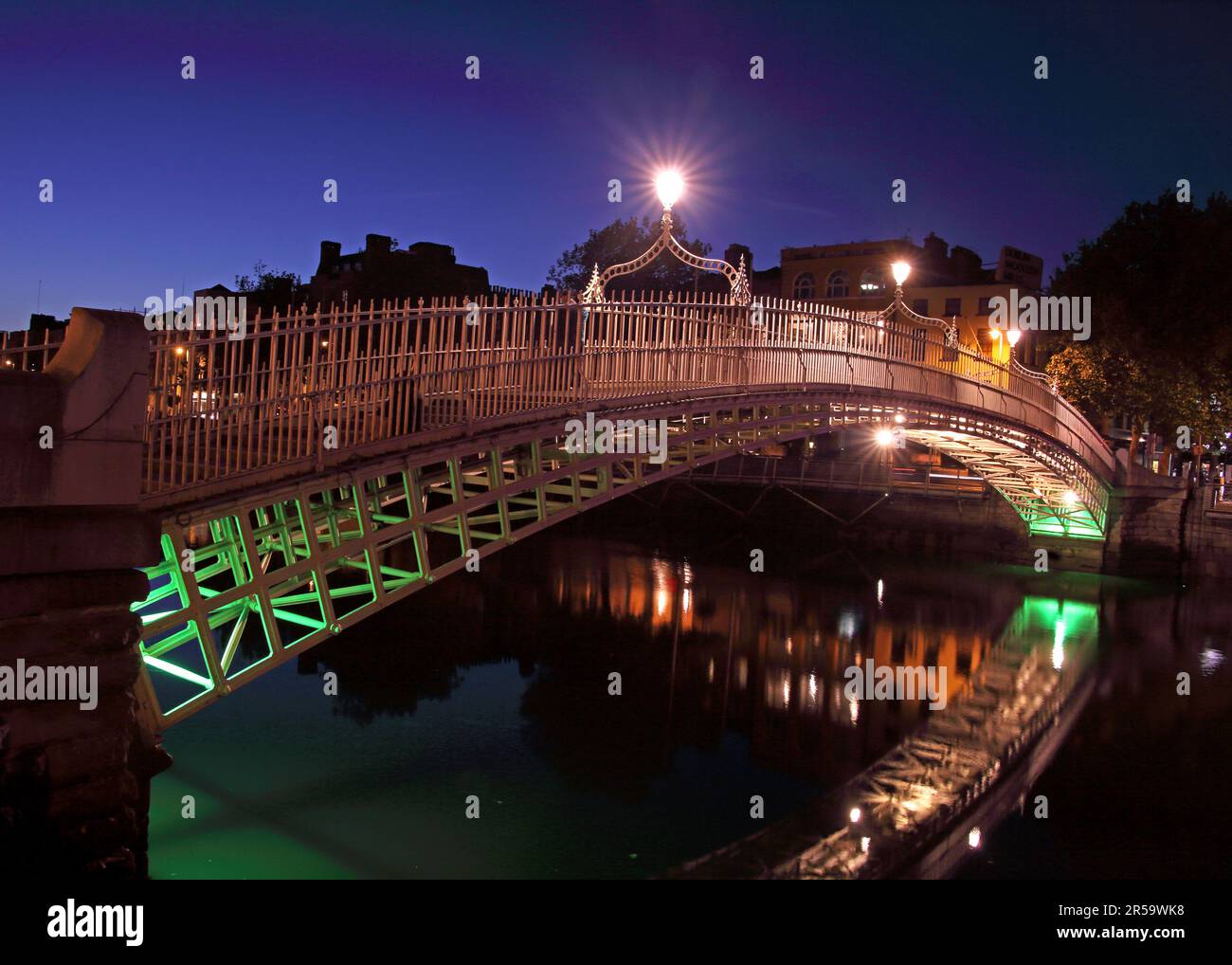 The Ha’penny Bridge illuminated at night spanning the River Liffey in Dublin city centre, Ireland, with reflections visible on the water Stock Photo