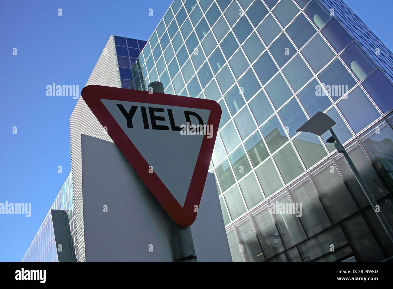 Yield road sign positioned outside the Grand Canal Theatre, now Bord Gáis Energy Theatre, at Grand Canal Dock in Dublin, Ireland, with modern glass Stock Photo