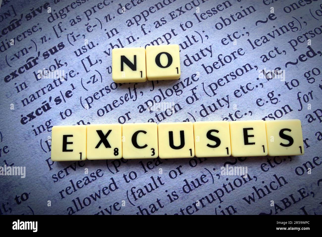 “No Excuses” spelled using Scrabble-style letter tiles placed on an open dictionary page,representing motivation, accountability and personal response Stock Photo