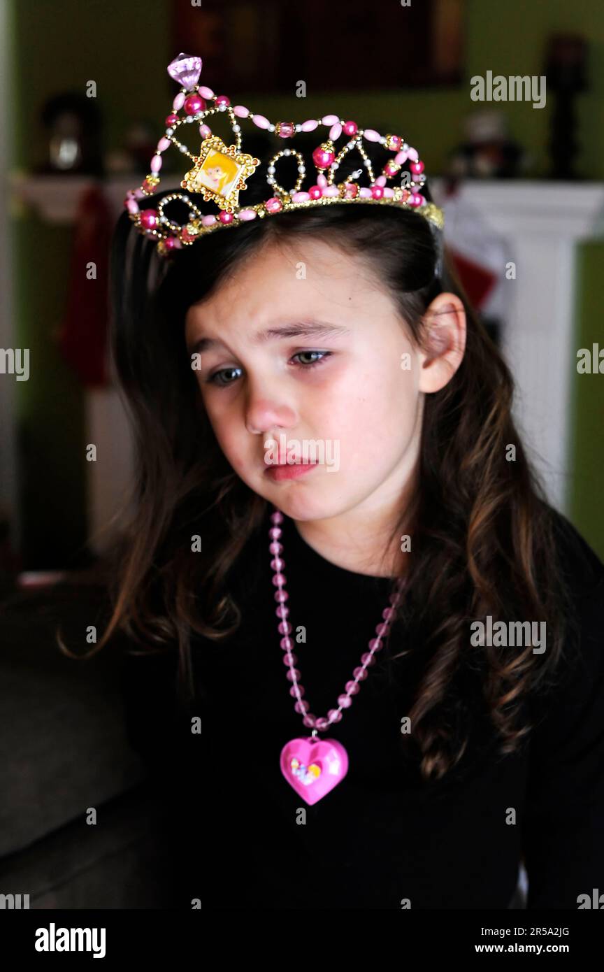 A young girl looks sad wearing toy princess accessories. Stock Photo