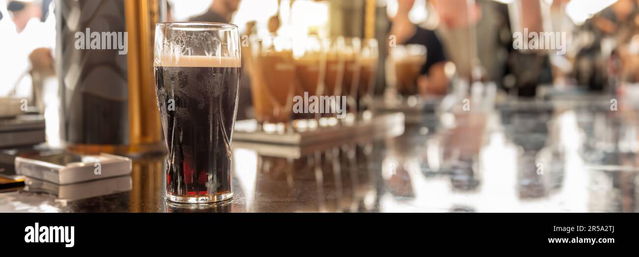 Glasses of stout beer on a bar counter, blurred people, panoramic pub header Stock Photo
