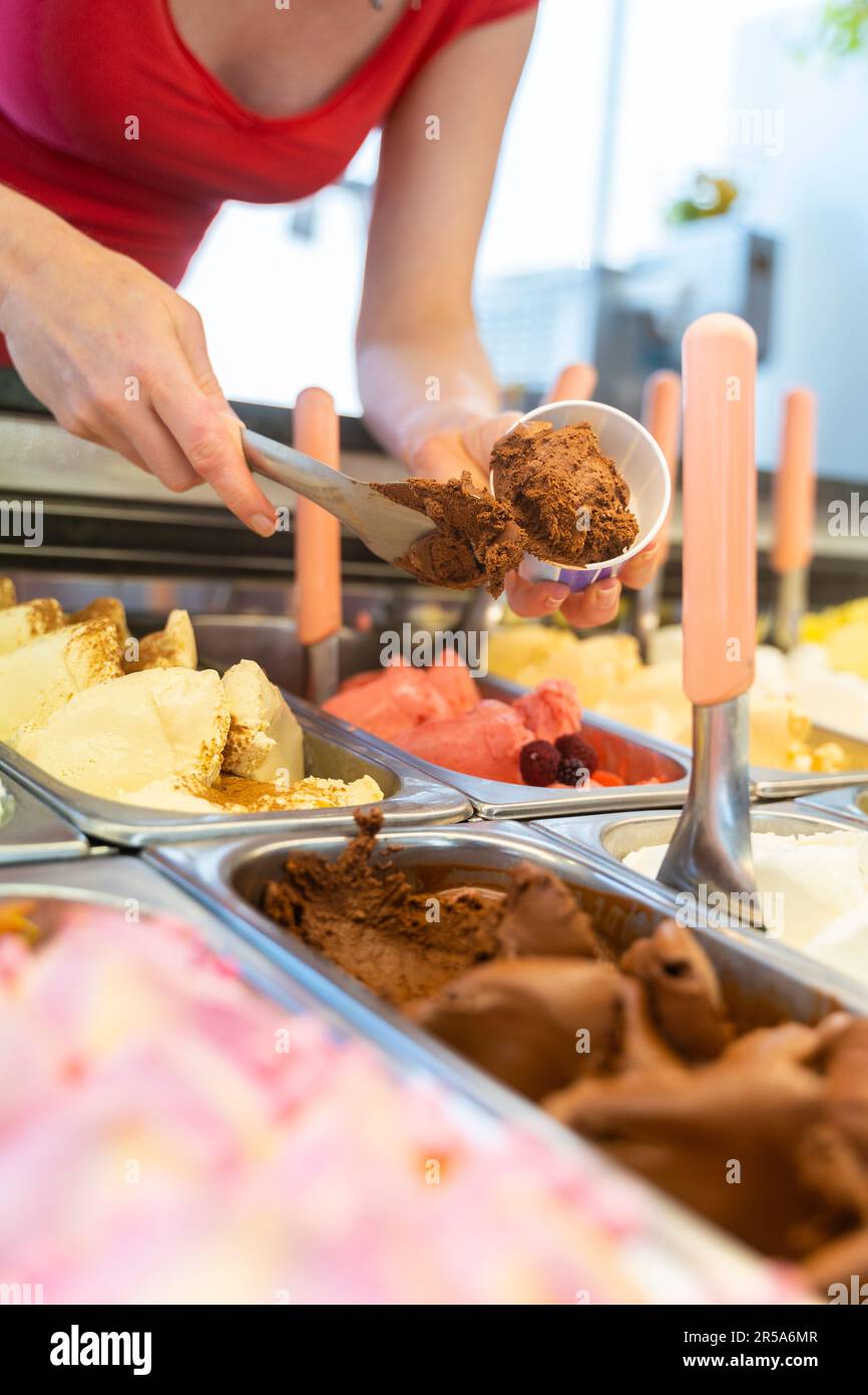 Ice cream showcase with a saleswoman preparing a chocolate flavored tub Stock Photo