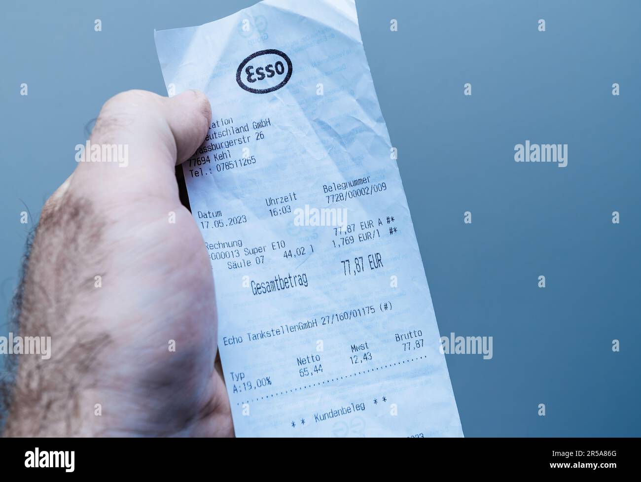 Germany - MAy 30, 2023: A male hand holding a paper receipt against a blue close-up background from the Esso gas station. Stock Photo