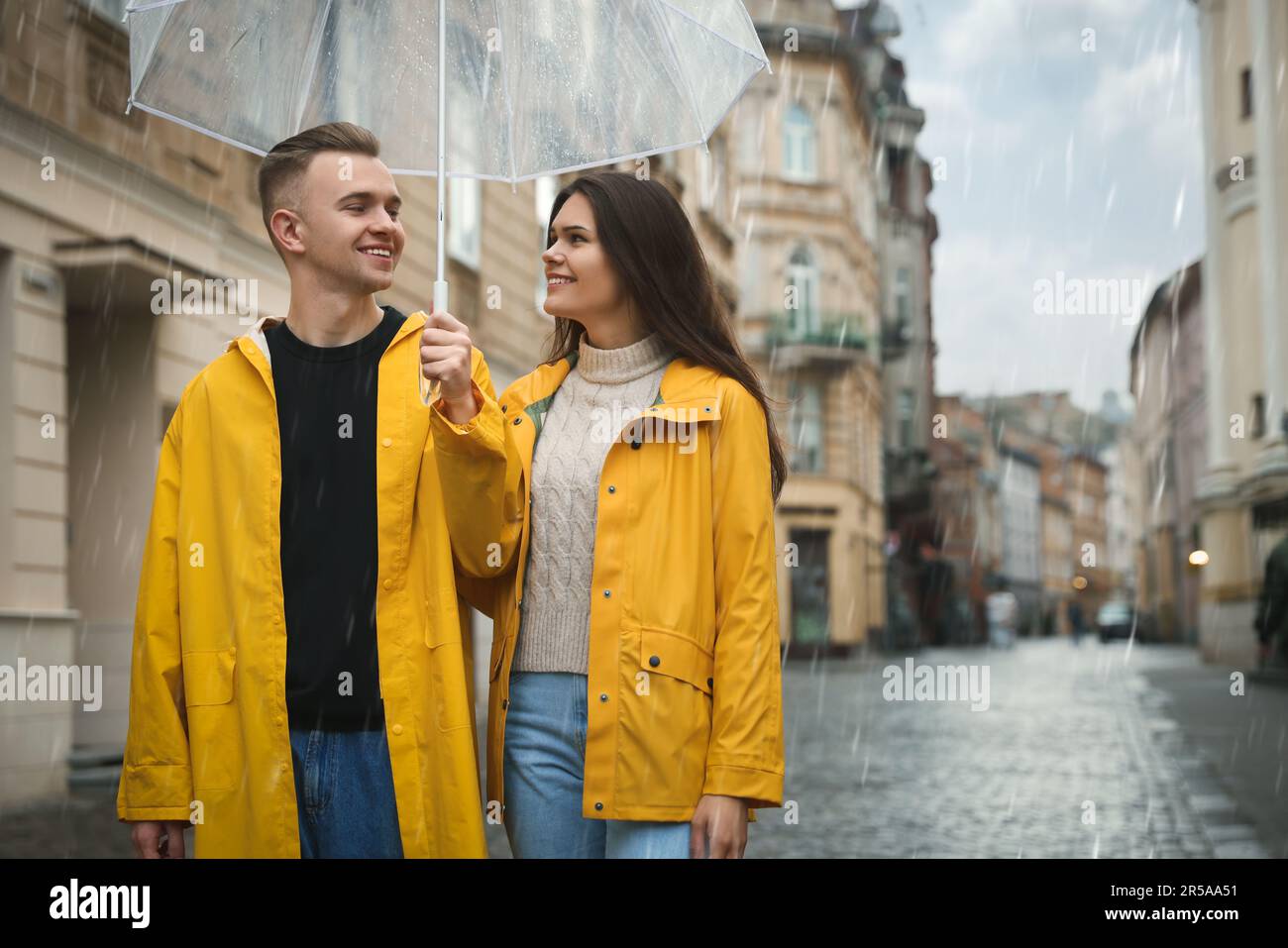 Lovely young couple with umbrella walking under rain on city street ...