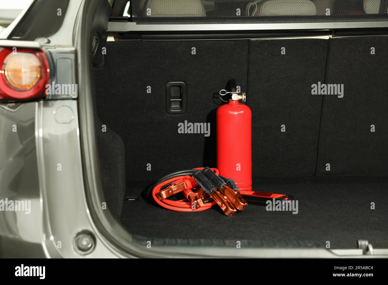 Red fire extinguisher and battery jumper cables in trunk. Car safety Stock Photo Alamy