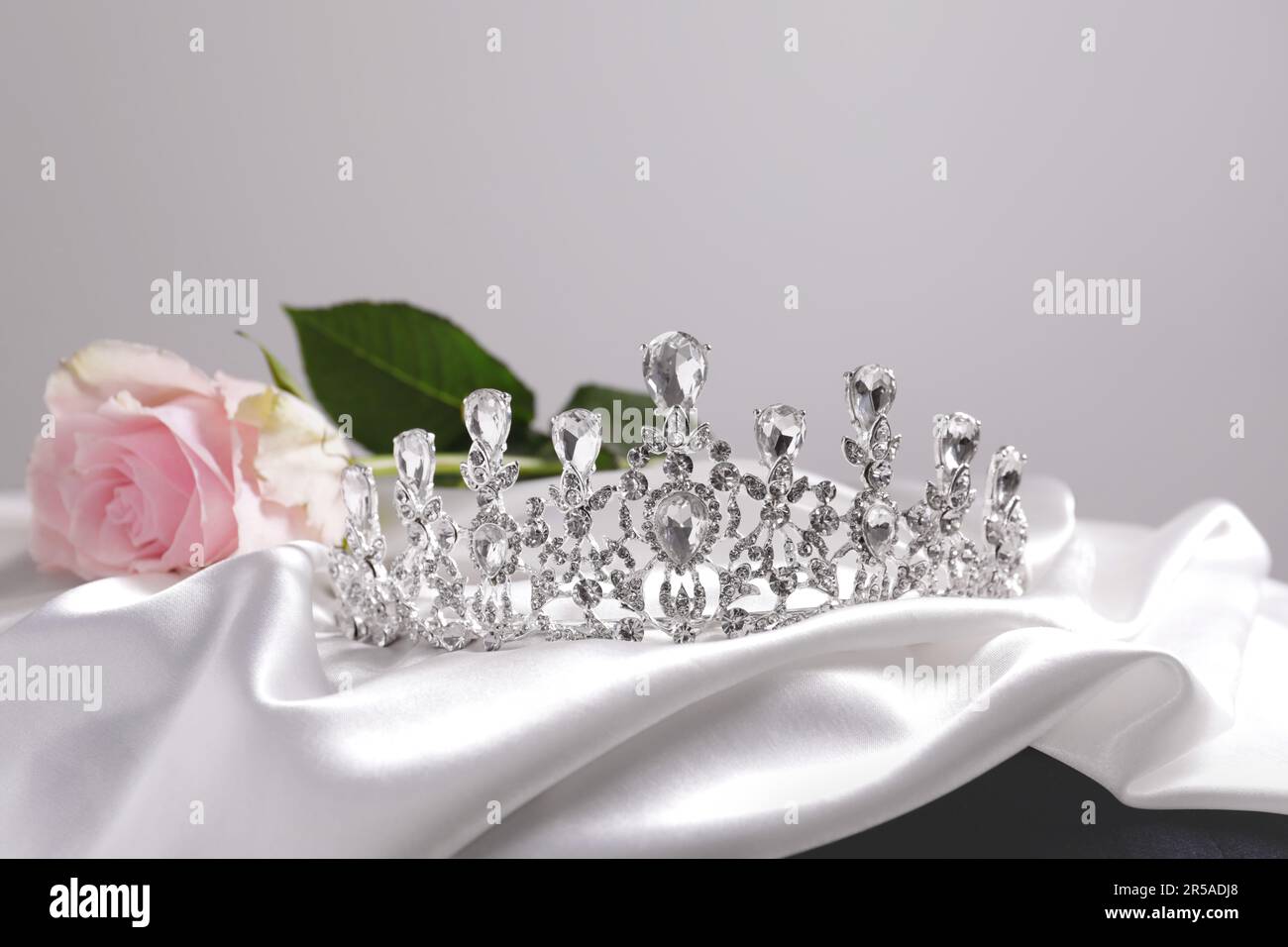 Beautiful silver tiara with diamonds and rose on white silk cloth Stock Photo