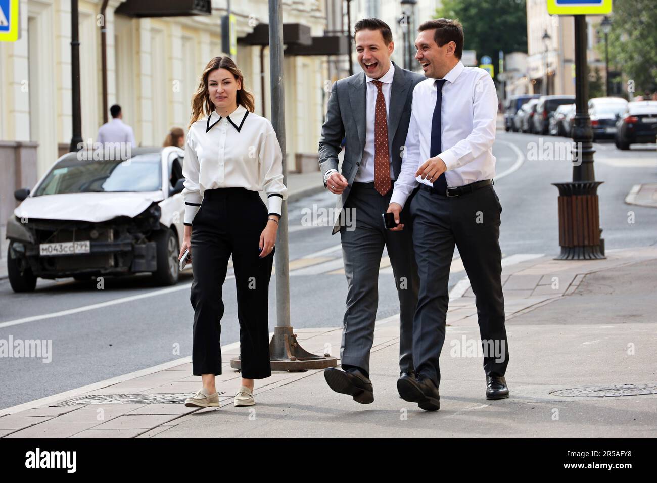 Office employees walking down the city street. Two laughing men in а business suites and stylish woman together, concept of successful people, partner Stock Photo