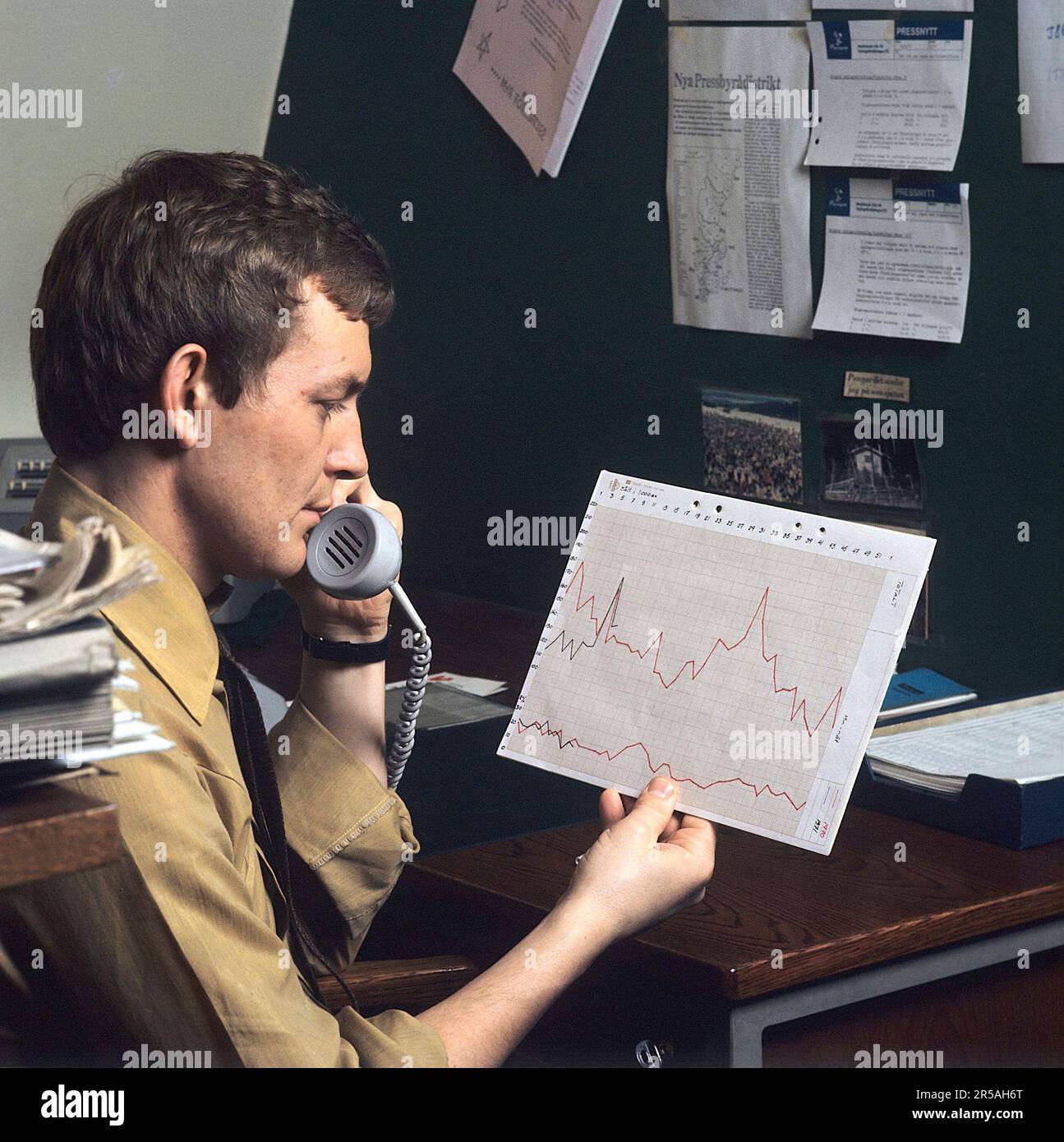 Office in the 1970s. A man is holding a document showing a chart diagram that shows the variety in sales during a certain period of time. Sweden 1971 Stock Photo