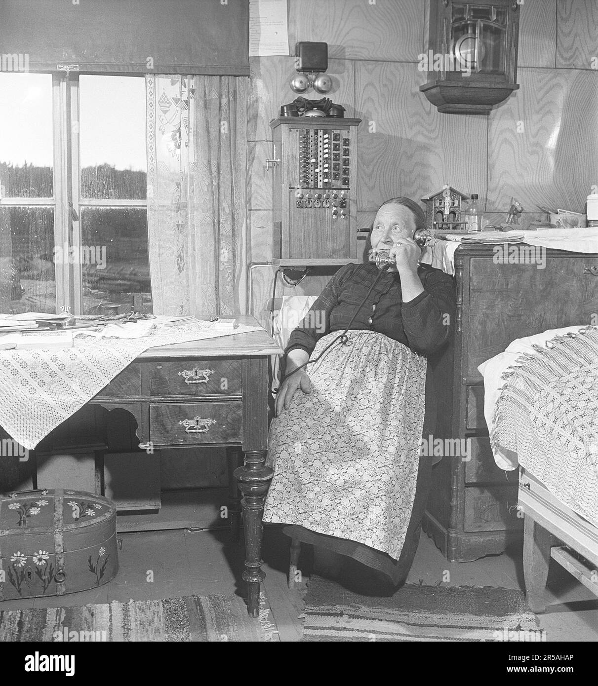 An elderly woman in Norrbotten's sparsely populated area at home in the room by the telephone switchboard that is mounted on the wall. It was common in the villages in sparsely populated areas that someone had the telephone switchboard at home and was responsible for connecting the telephone calls from and to the residents of the village. You could also go here and call if you didn't have a phone. Sweden 1949. Kristoffersson ref AS75-4 Stock Photo