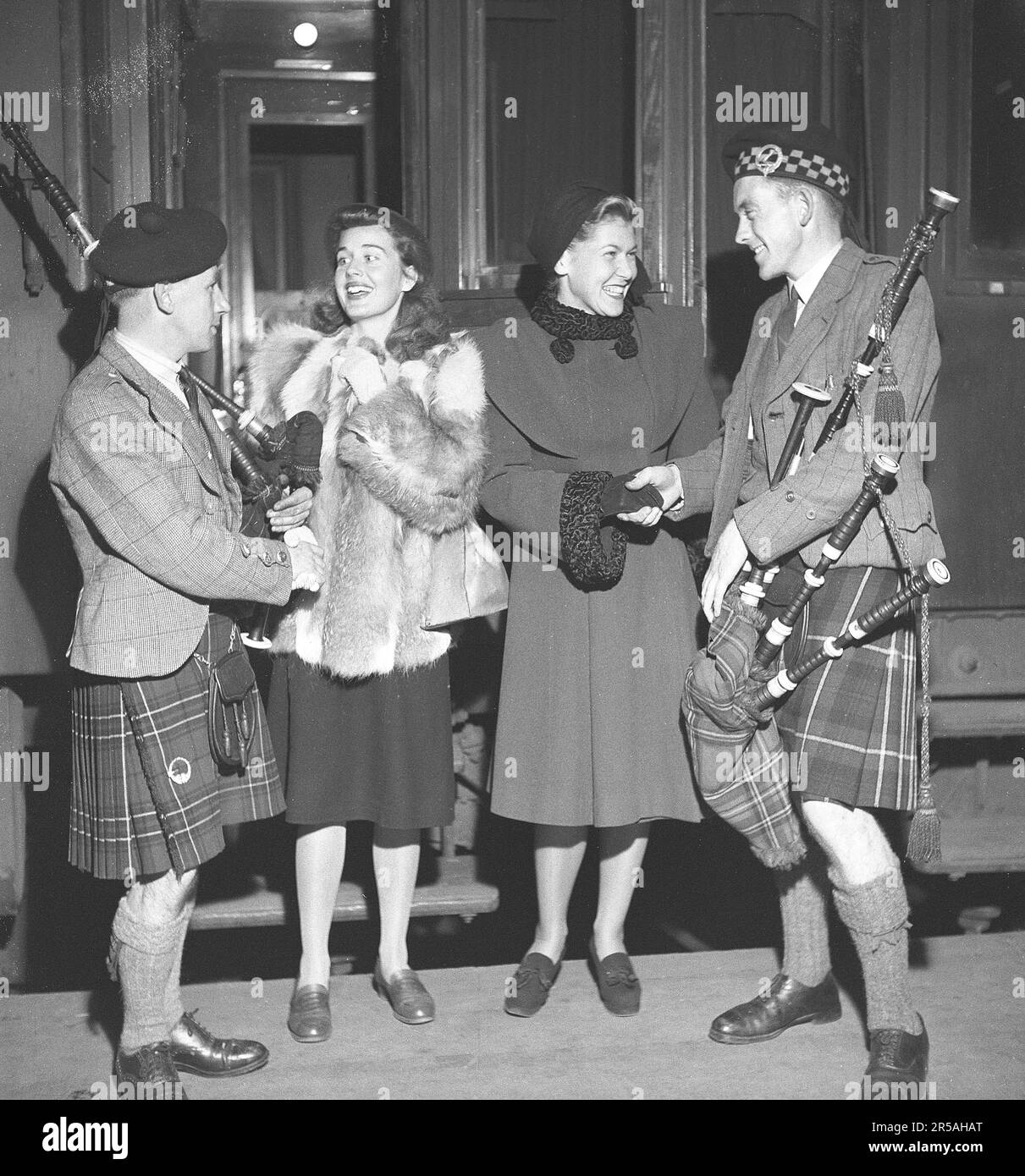 Young women happily greet musicians from Scotland, dressed in traditional kilts with bagpipes. It is Agneta Lagerfelt and Ingrid Eksell from the Oscarsteatern in Stockholm who welcome Donald MacLean and John MacFadyen who will participate in the stage set of Brigadoon.  Pipe Major Donald Maclean, Seaforth Highlanders, was a noted piper and composer during the mid-20th century. He won both Gold Medals (Oban, 1951, MacDonald’s Salute, and Inverness, 1953, Black Donald’s March), and was renowned as a performer of light music.  John MacFadyen was born in Glasgow in 1926 to island parents.   John w Stock Photo
