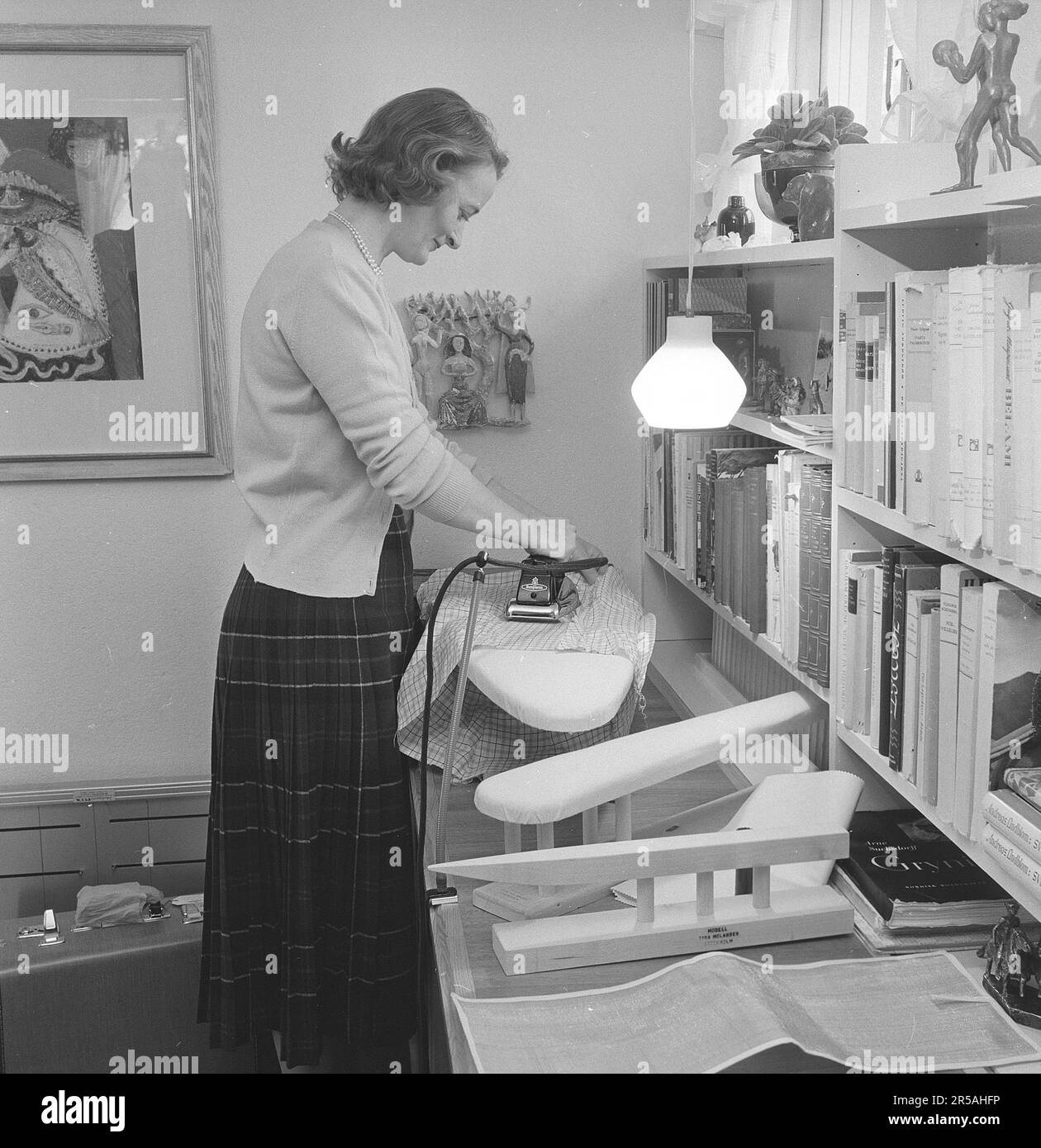 Ironing in the 1950s. A woman seen ironing her clothes at home. Perhaps prior a holdiay trip as her suitcase is seen standing on the floor beside her. She is Mrs. Blomberg living in Lidingö Stockholm.  Sweden march 1956 Stock Photo