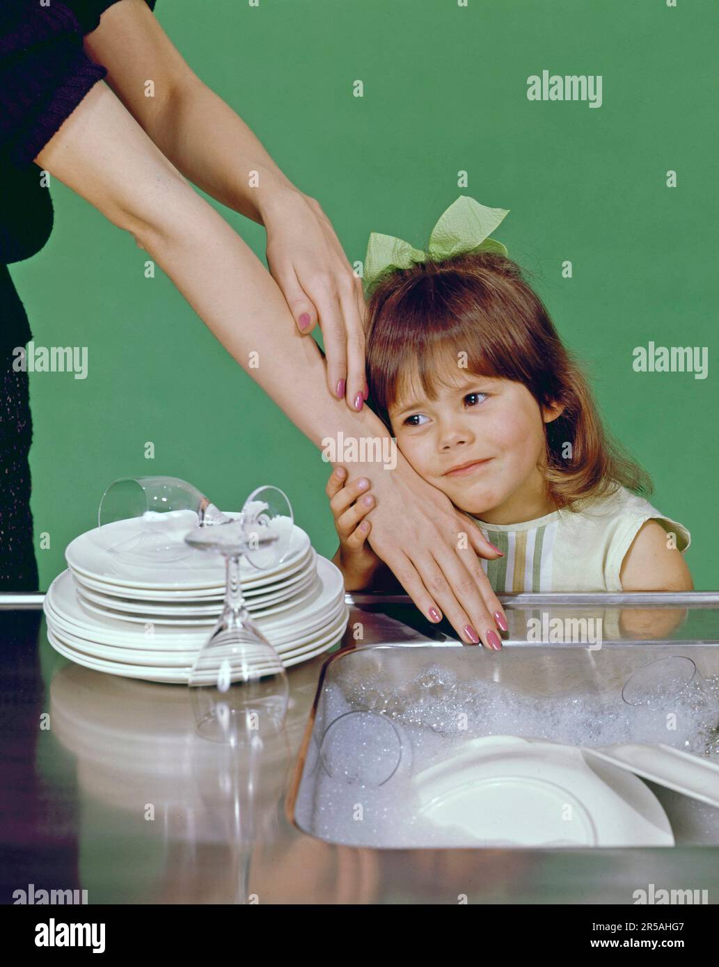 In the 1960s. A little girl pictured with her mother at a kitchen-sink, having her chin agains her mothers arm and hand, feeling the softness. Sweden 1965 Stock Photo