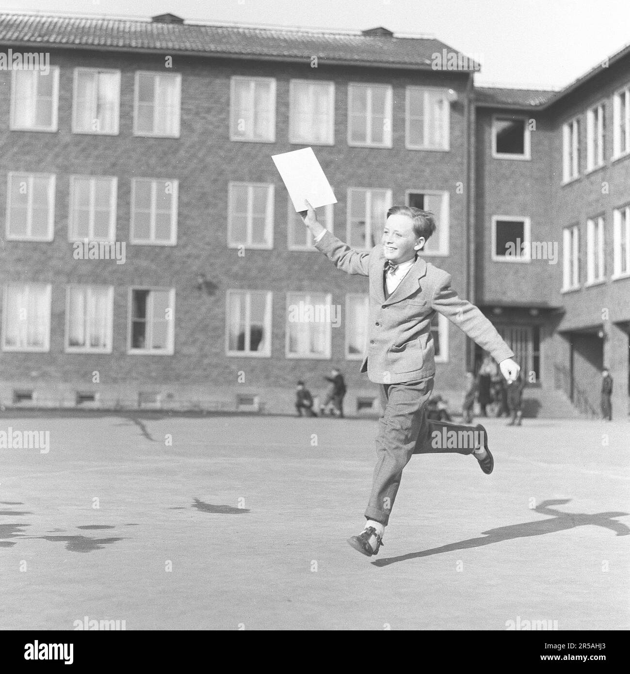The last school day. The boy jumps happily on his last school day for the term, holding his grade paper in the hand. Well dressed as children were in the 1950s decade. Sweden 1950s. ref BV40-11 Stock Photo