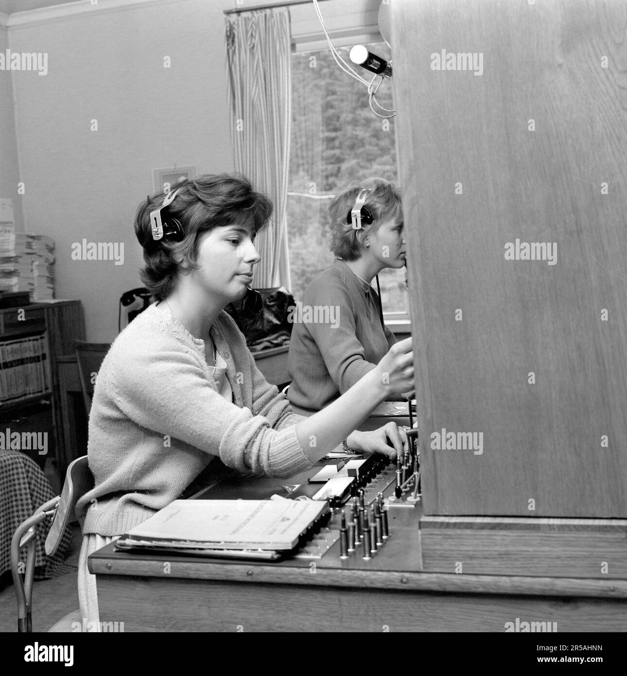 Telephony in the 1960s. Woman working at a telephone switchboard as it's operator. A telephone communication system that was manually operated where the incoming calls were forwarded and redirected to the another telephone number by the operator, in this case locally within the building serving a company or an organization with many internal telephone lines. The switchboard operator could take messages, put you on hold if the line was busy. Sweden 1963 Stock Photo