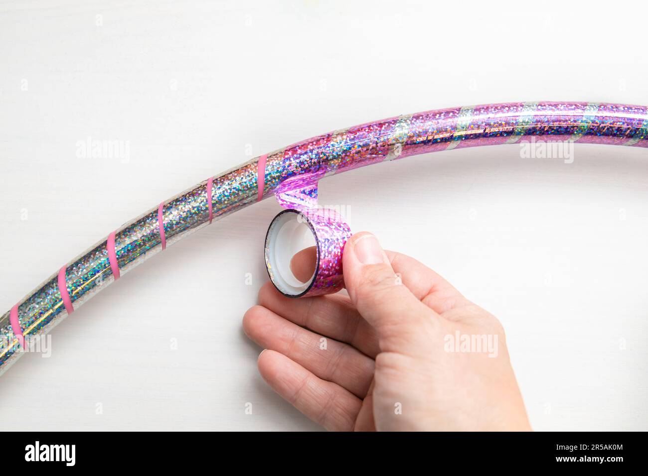 Person hand decorate rhythmic gymnastics hula hoop with pink shiny glitter decorative adhesive tape. Stock Photo