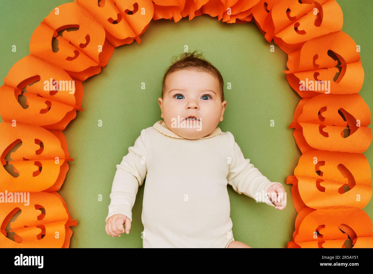 Halloween portrait of adorable baby lying on green background next