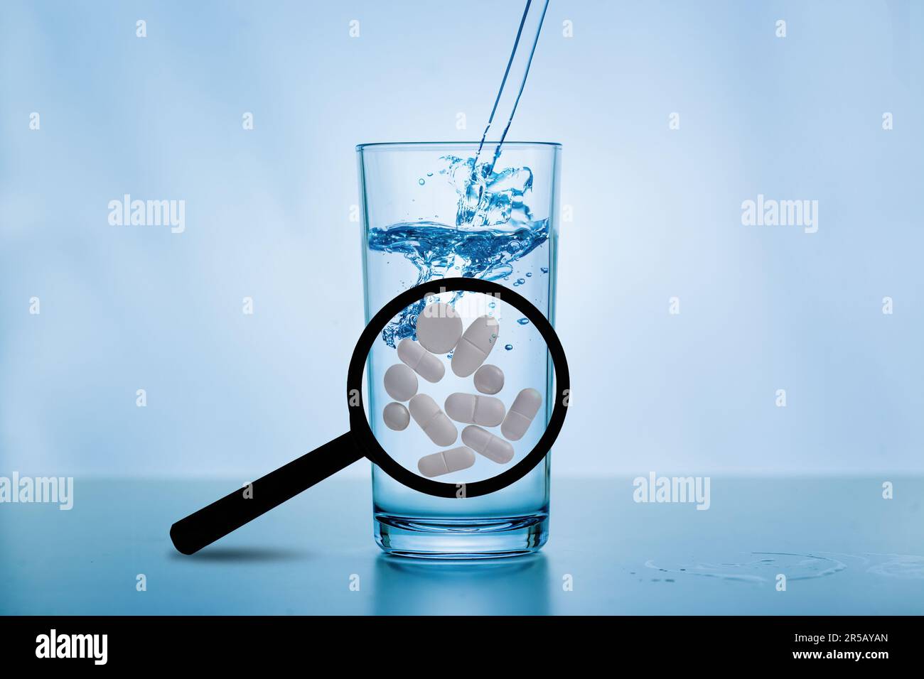 A magnifying glass with large white tablets in front of a glass of