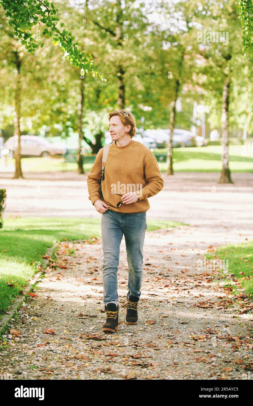Outdoor portrait of handsome young man walking outside through public ...