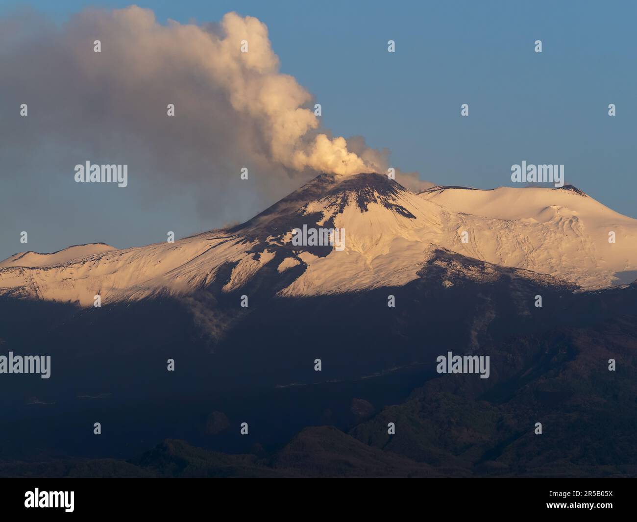 Snow capped Mount Etna at sunrise, releasing smoke the day after an