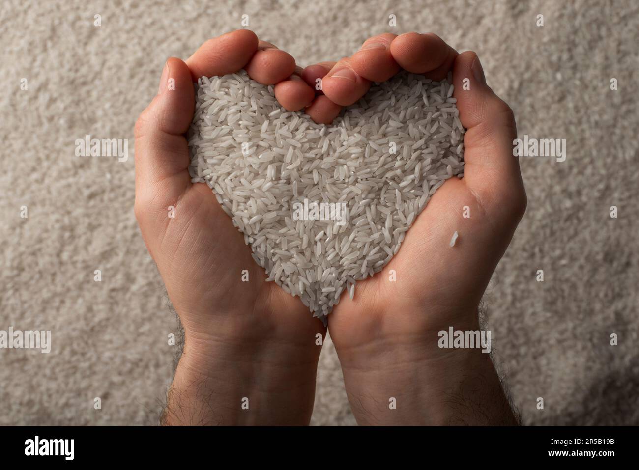 Human hands in shape of heart holding handful of rice on rice background Stock Photo
