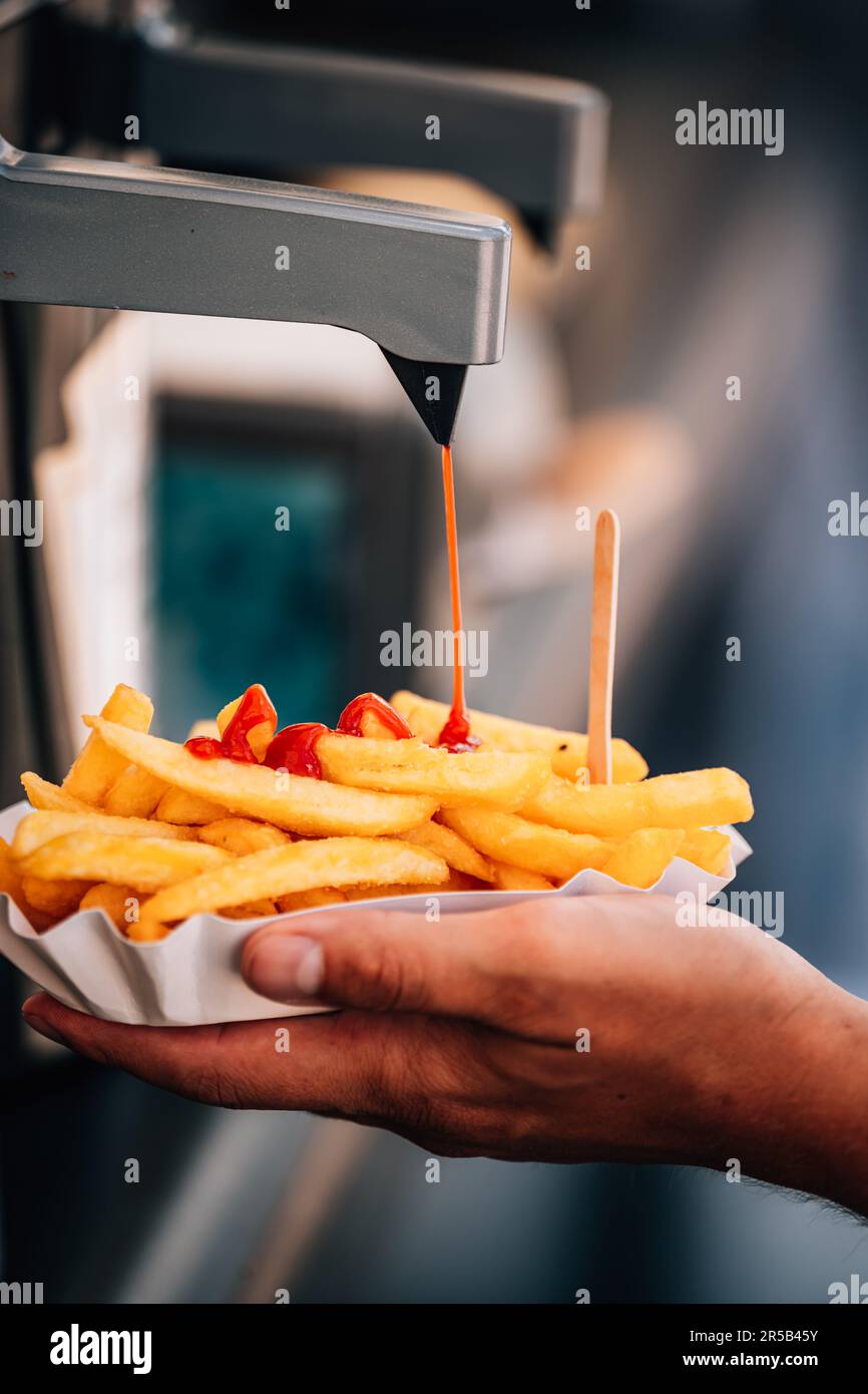 A vertical shot of a person pouring ketchup on French fries Stock Photo