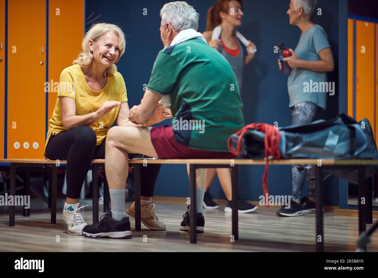Mature man and woman facing each other while sitting in gym locker room and talking before training. Health concept. Stock Photo