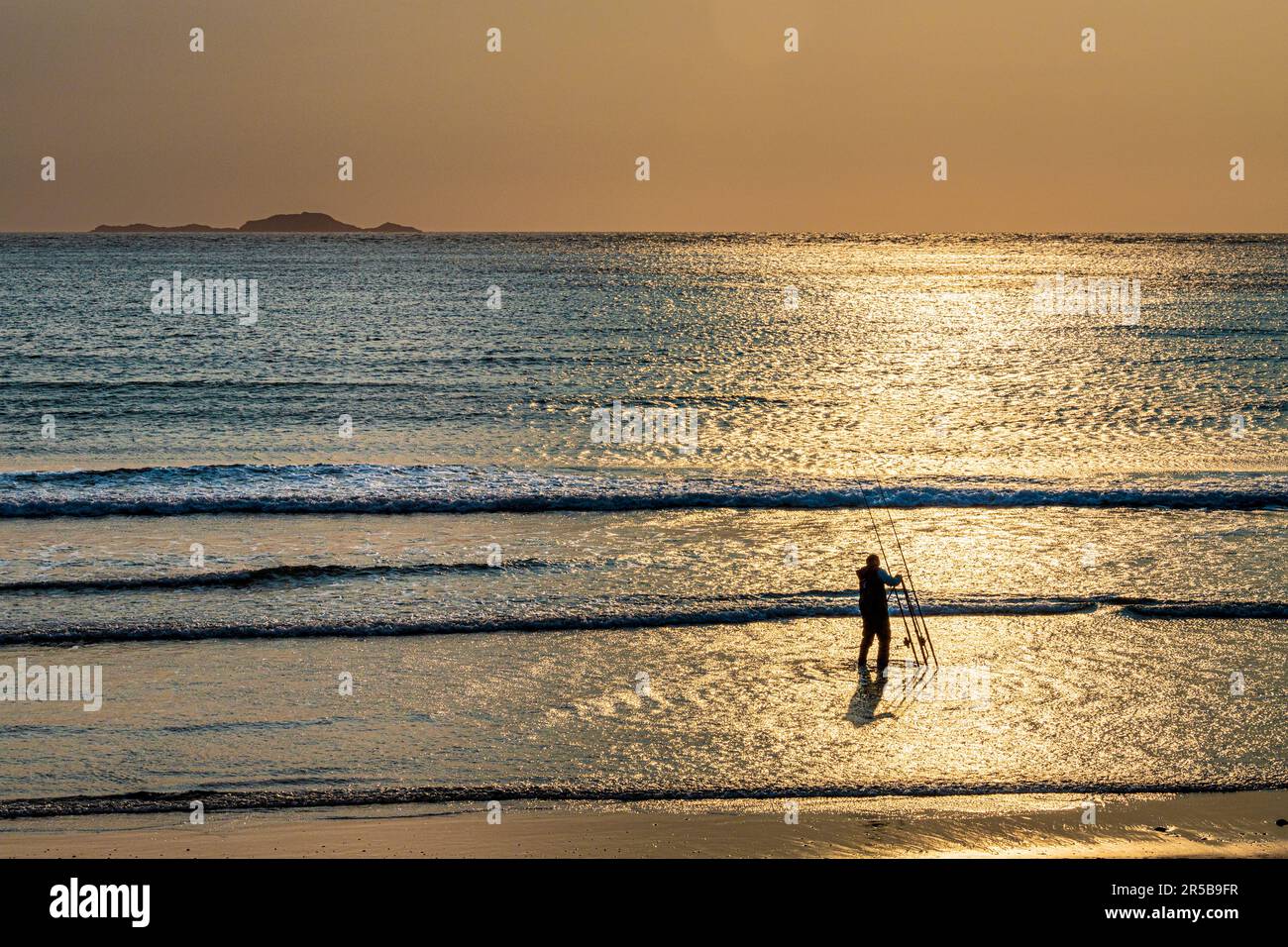 A sea angler beach casting in the sunset at Whitesands Bay, a Blue Flag beach on the St David's peninsula in the Pembrokeshire Coast National Park, Wa Stock Photo