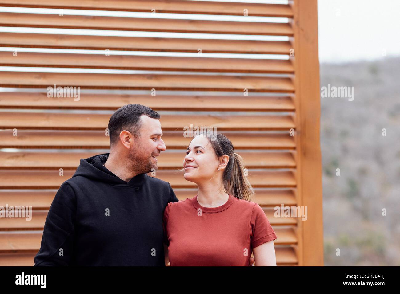 Attractive man and beautiful woman look at each other and smile. Young cheerful couple hugging outdoors. Happy family in mountain park spend time toge Stock Photo