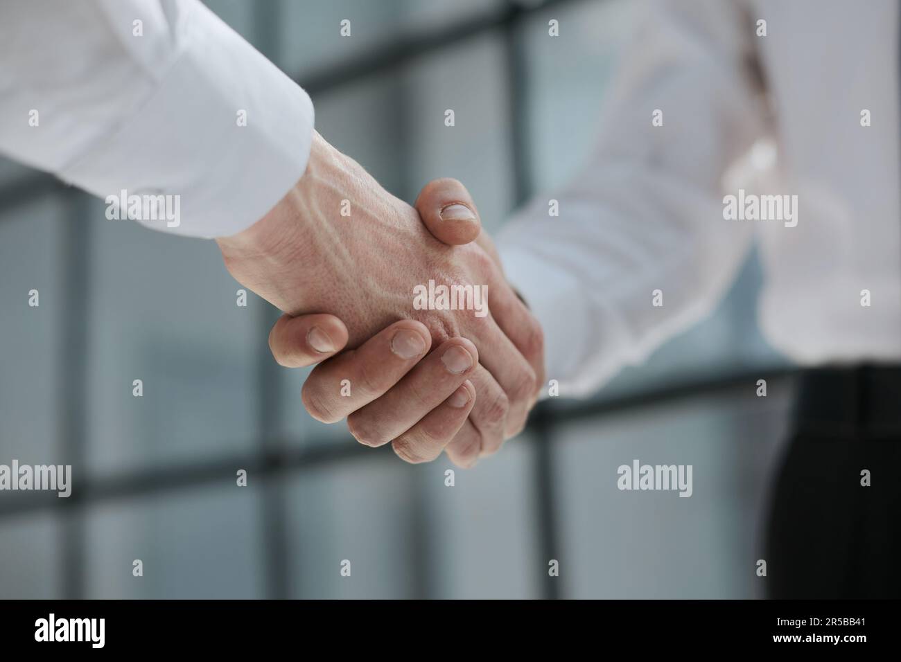 Two businessmen shake hands on the background of empty modern office, signing of a contract concept Stock Photo