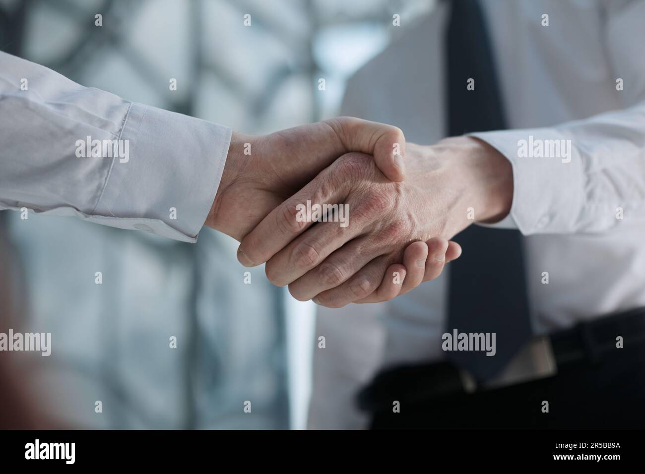 Two businessmen shake hands on the background of empty modern office, signing of a contract concept Stock Photo