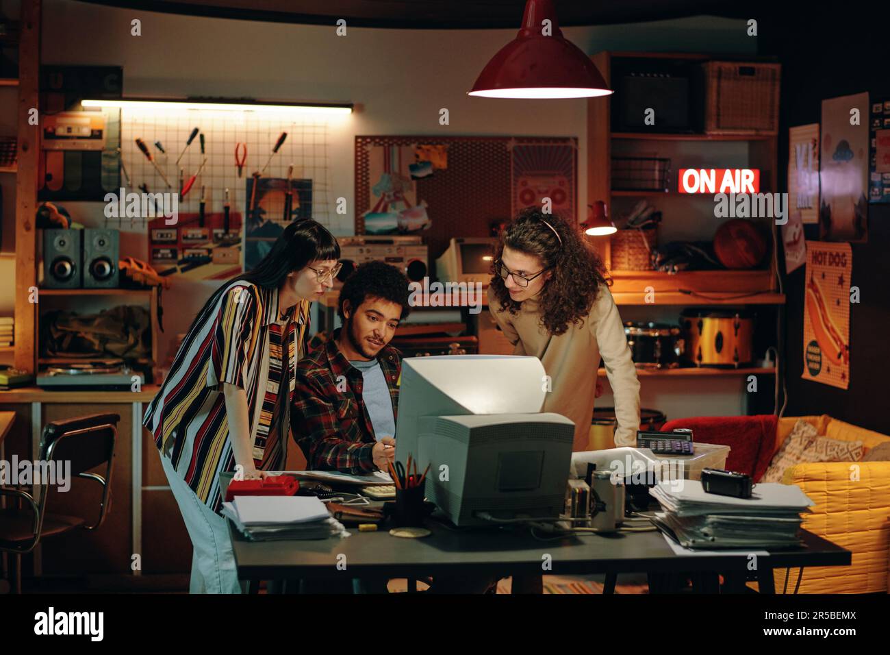 Group of young people sitting at table in front of computer and discussing new project Stock Photo