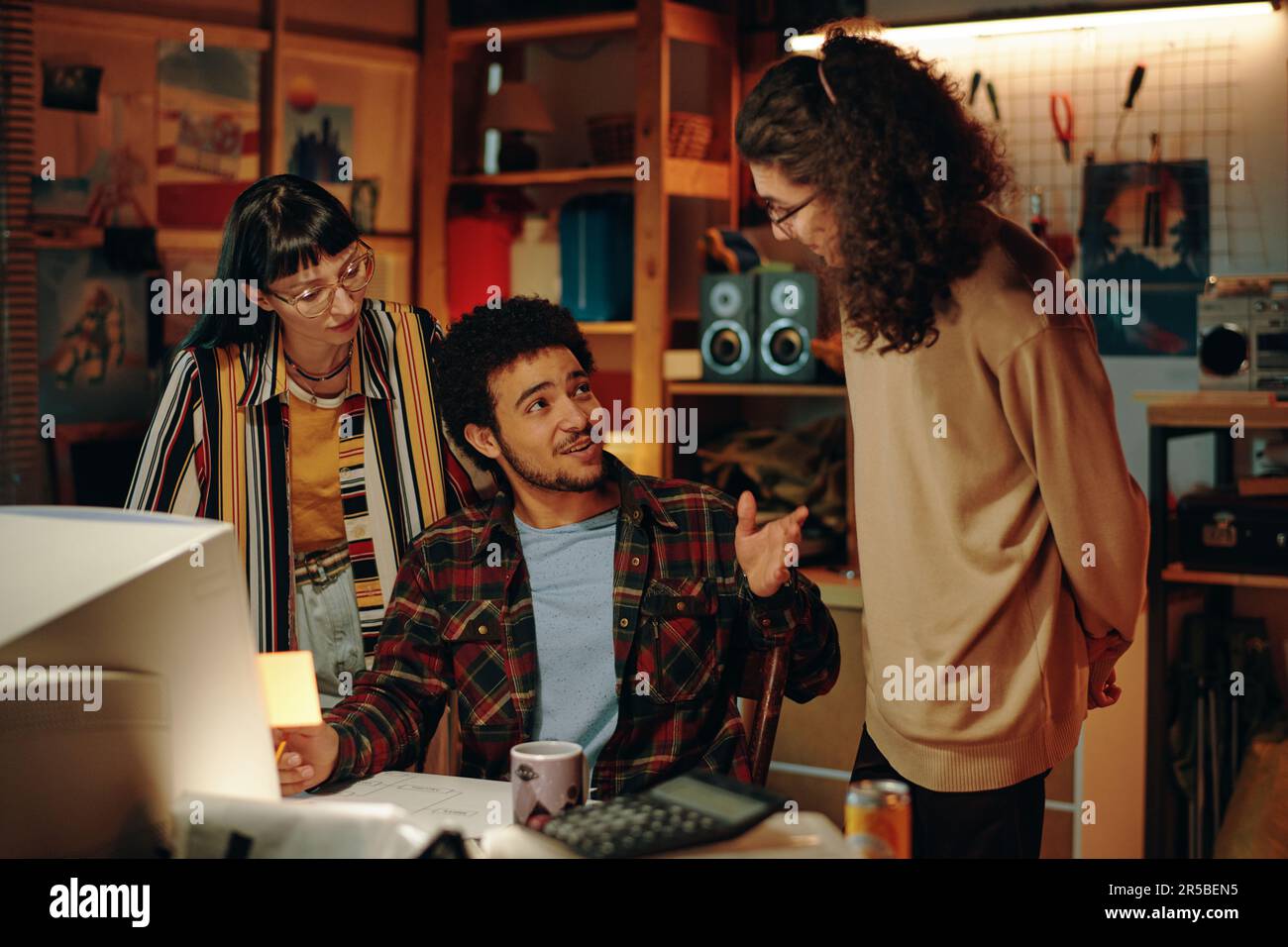 Young guy discussing new idea with his colleagues while working on computer in garage Stock Photo